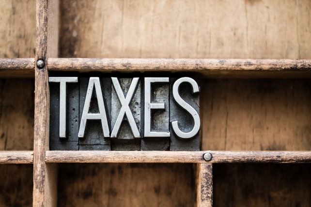 The word "TAXES" written in vintage metal letterpress type in a wooden drawer with dividers.